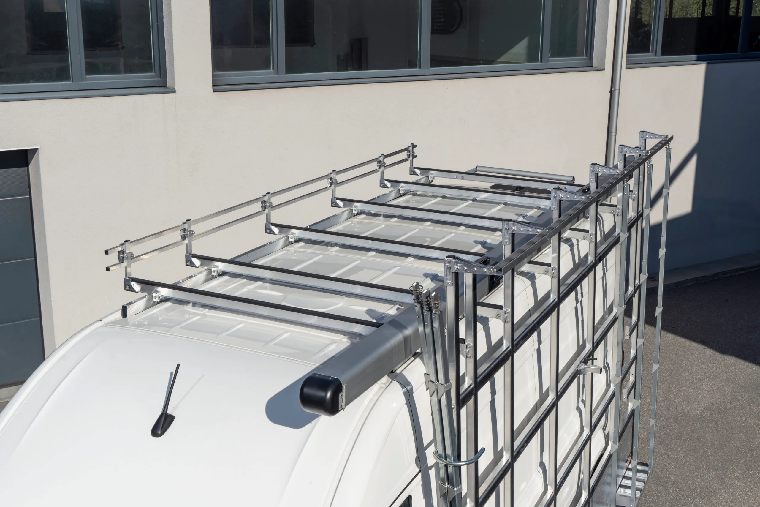 Dachträger als Gitterrost auf einem weissen Transporter, mit Leiterrolle über dem Heck und Aufstiegsleiter an der Hecktür