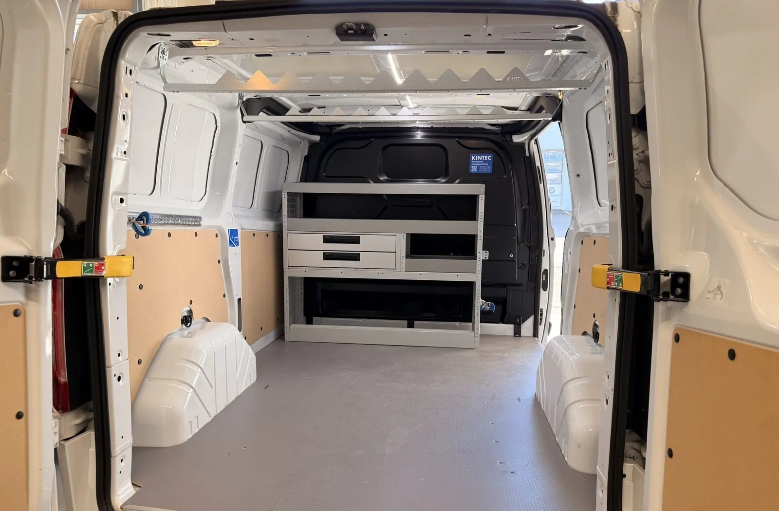 Blick durch die Hecktüren eines Ford Transit Custom: Sperrholz an den Wänden, Regal mit Schubladen an der Trennwand