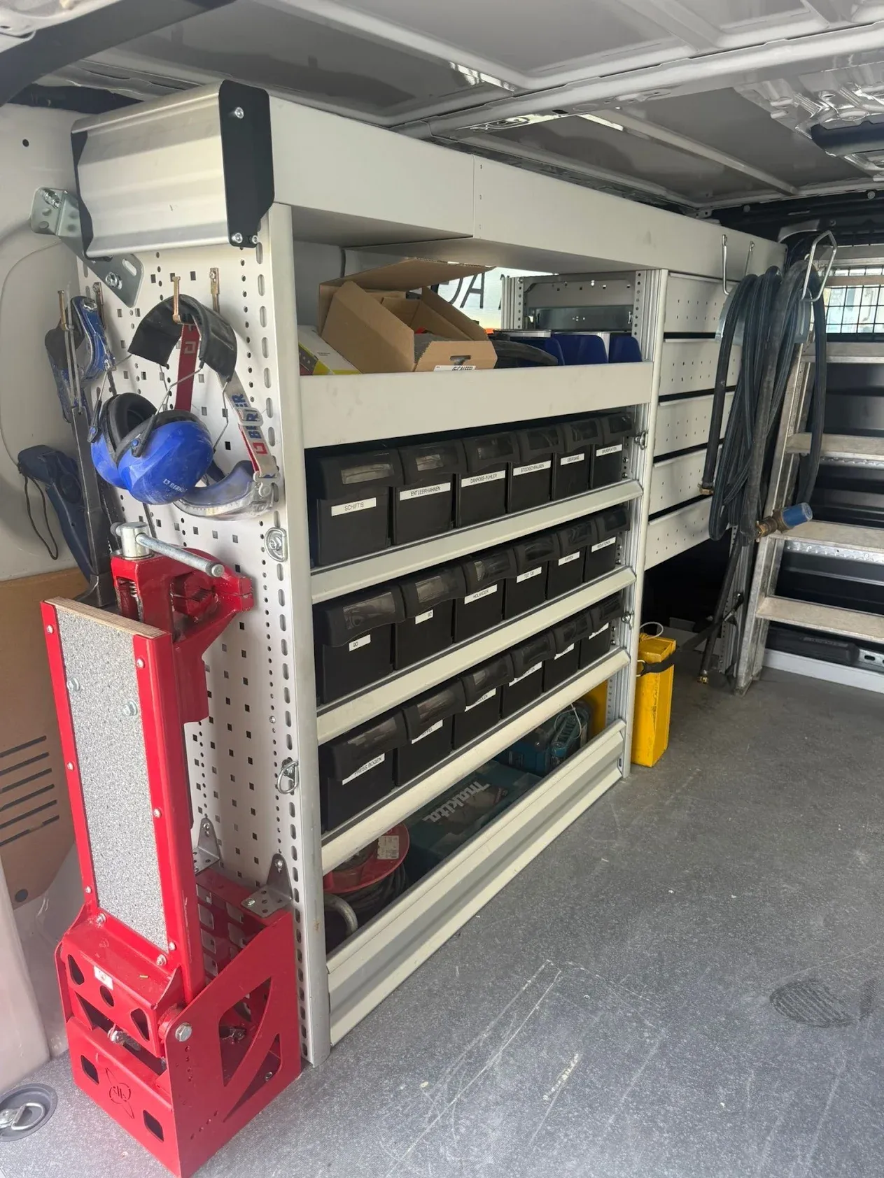 Regalzeile mit beschrifteten Kleinteilboxen, Lochwand mit Gehörschutz und montiertem Schraubstock im Laderaum