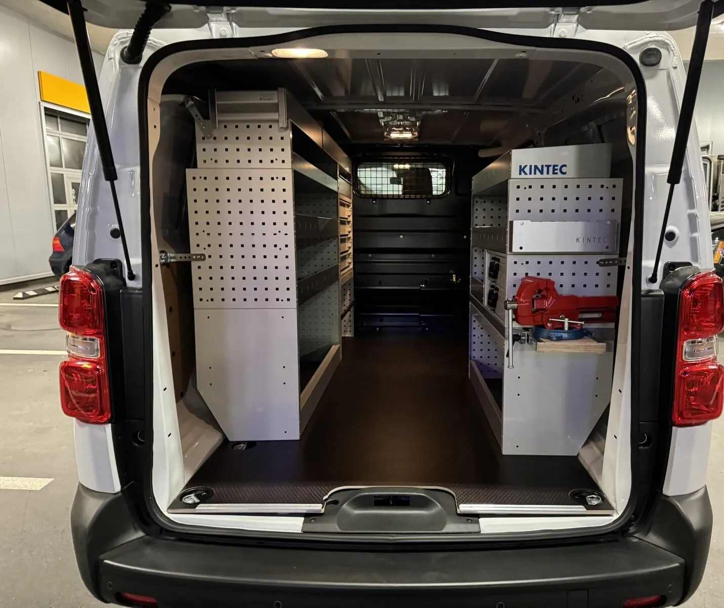 Peugeot Expert mit offenen Hecktüren: links ein Regal mit Fachböden, rechts kleine Schubladen und ein roter Schraubstock