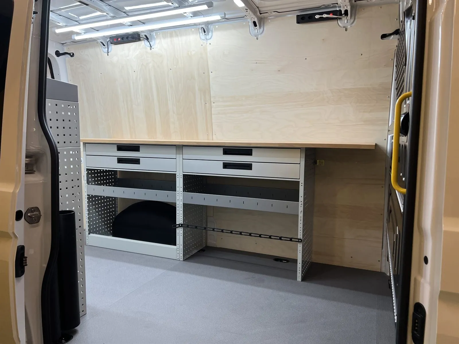 Werkbank mit Holzplatte und Schubladen im Crafter, Wände mit hellem Holz verkleidet, LED-Leisten an der Decke