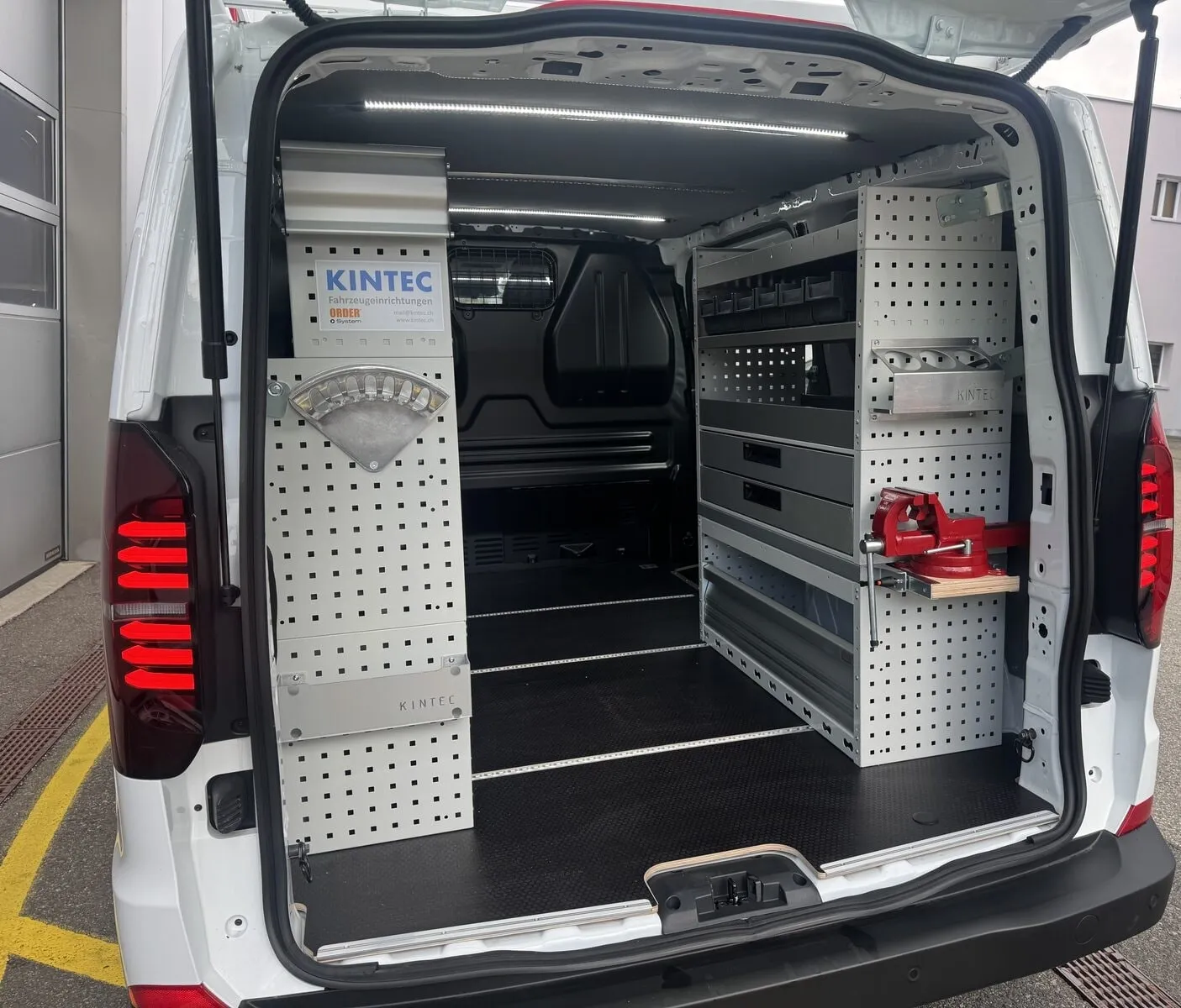 Geöffnete Heckklappe eines VW Transporter T7: links Lochwände, rechts ein Regal mit Schubladen und ein roter Schraubstock